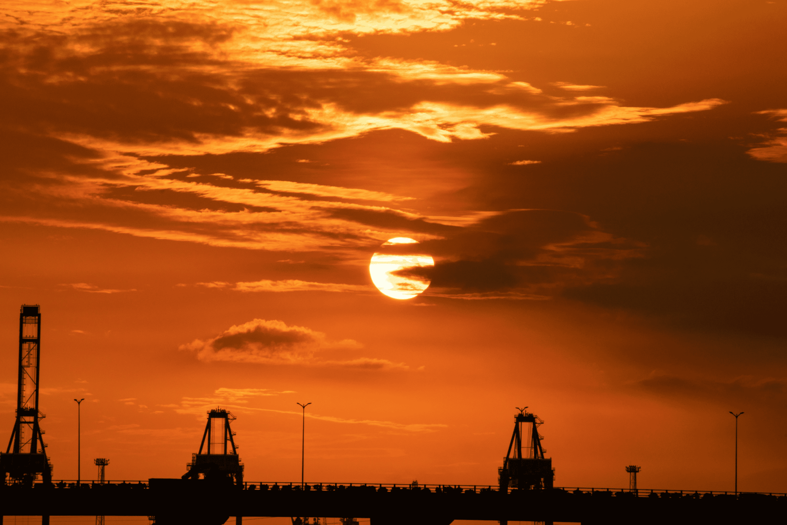 Sunset over oilfield with drilling rigs silhouetted against an orange sky.
